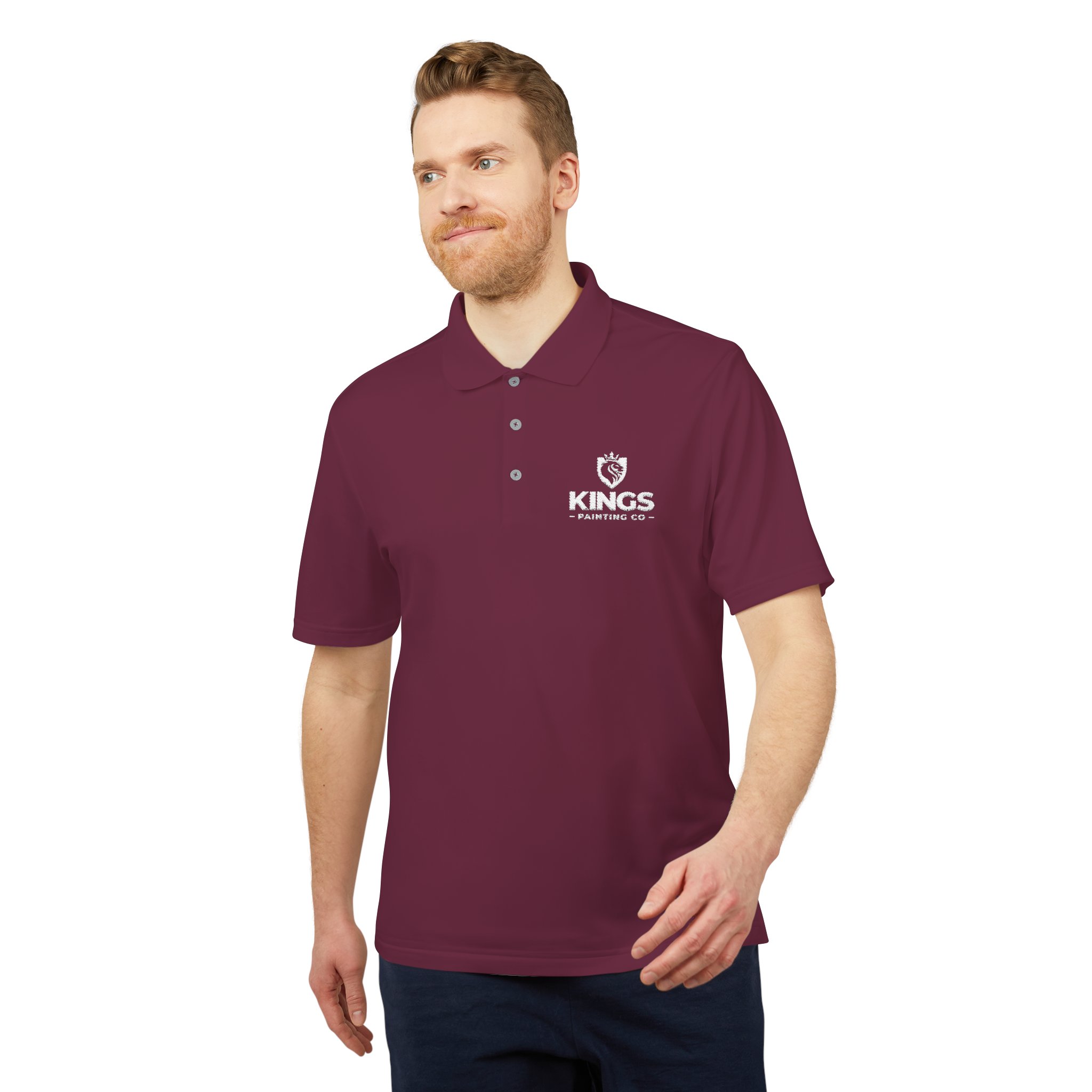 A man wearing a maroon Kings Painting Co. Performance Polo by Under Armour® featuring a white crown logo on the chest, standing against a plain white background.